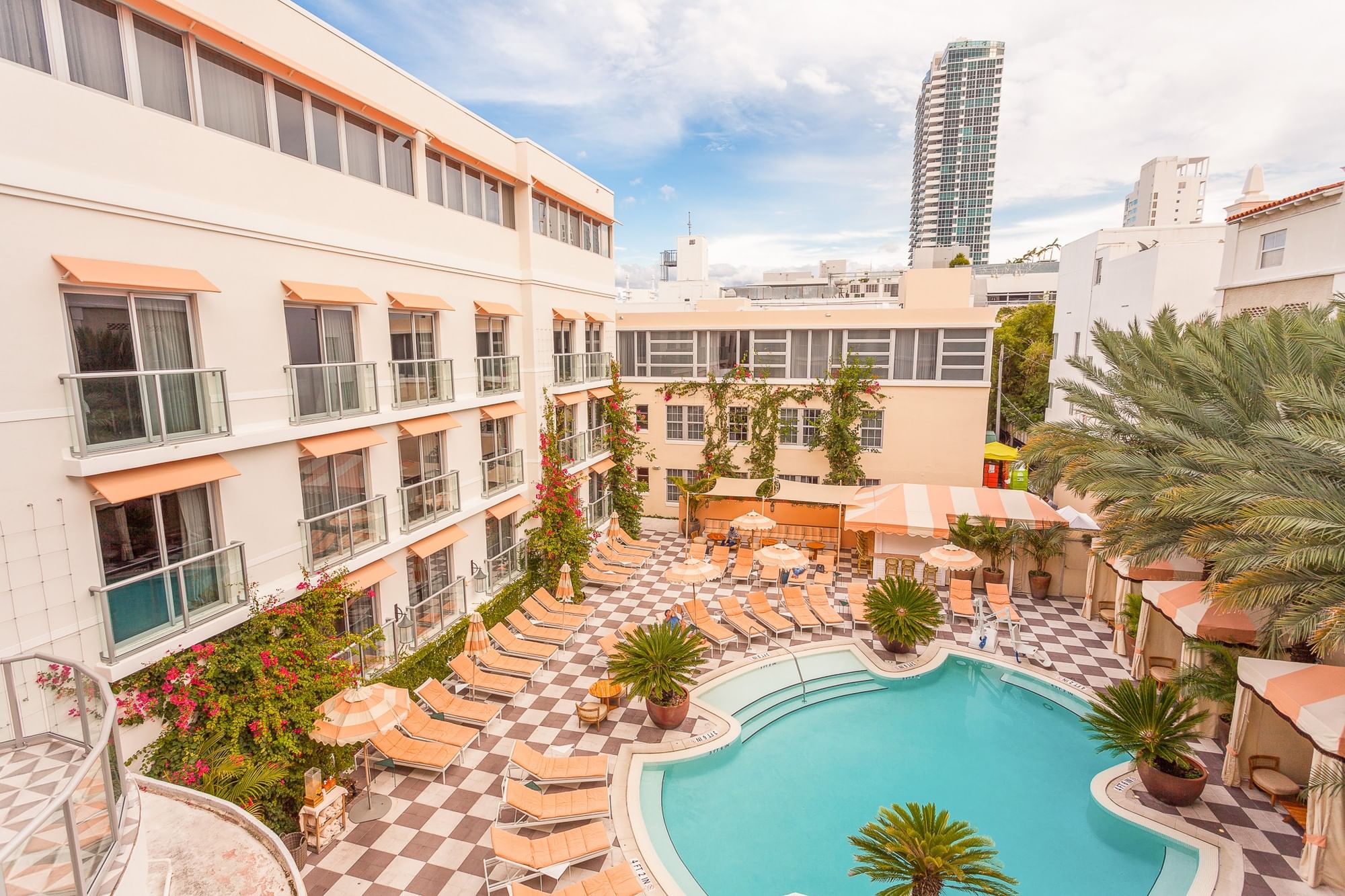 A large pool surrounded by lounge chairs and palm trees in front of a multi-story building.