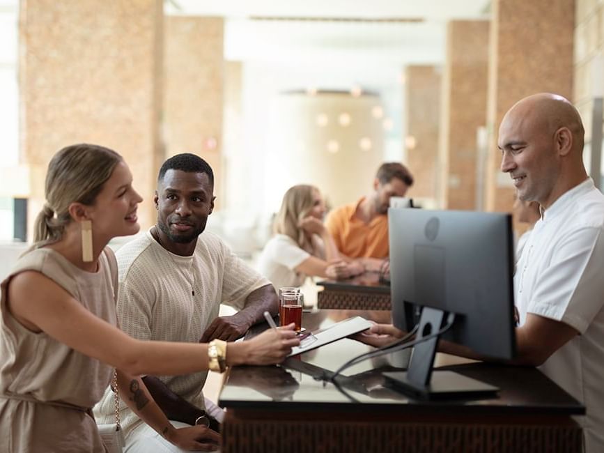 Individuals at a reception desk with a staff member behind a computer in Live Aqua Cancún