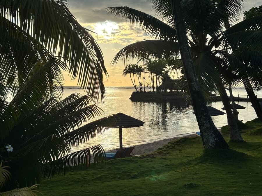 Beach view at sunset with palm trees and lounge chairs at Warwick Fiji Resort and Spa.