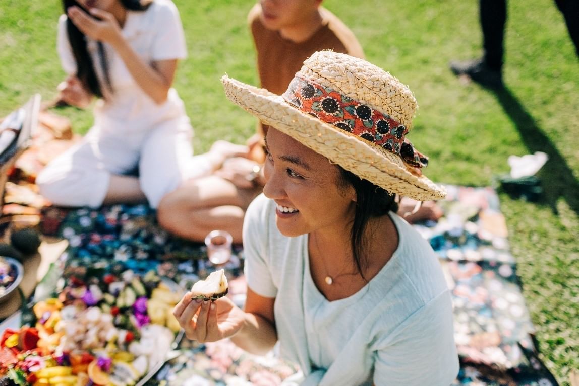 Woman wearing a straw hat and sitting on a picnic set-up at Fullerton Sydney