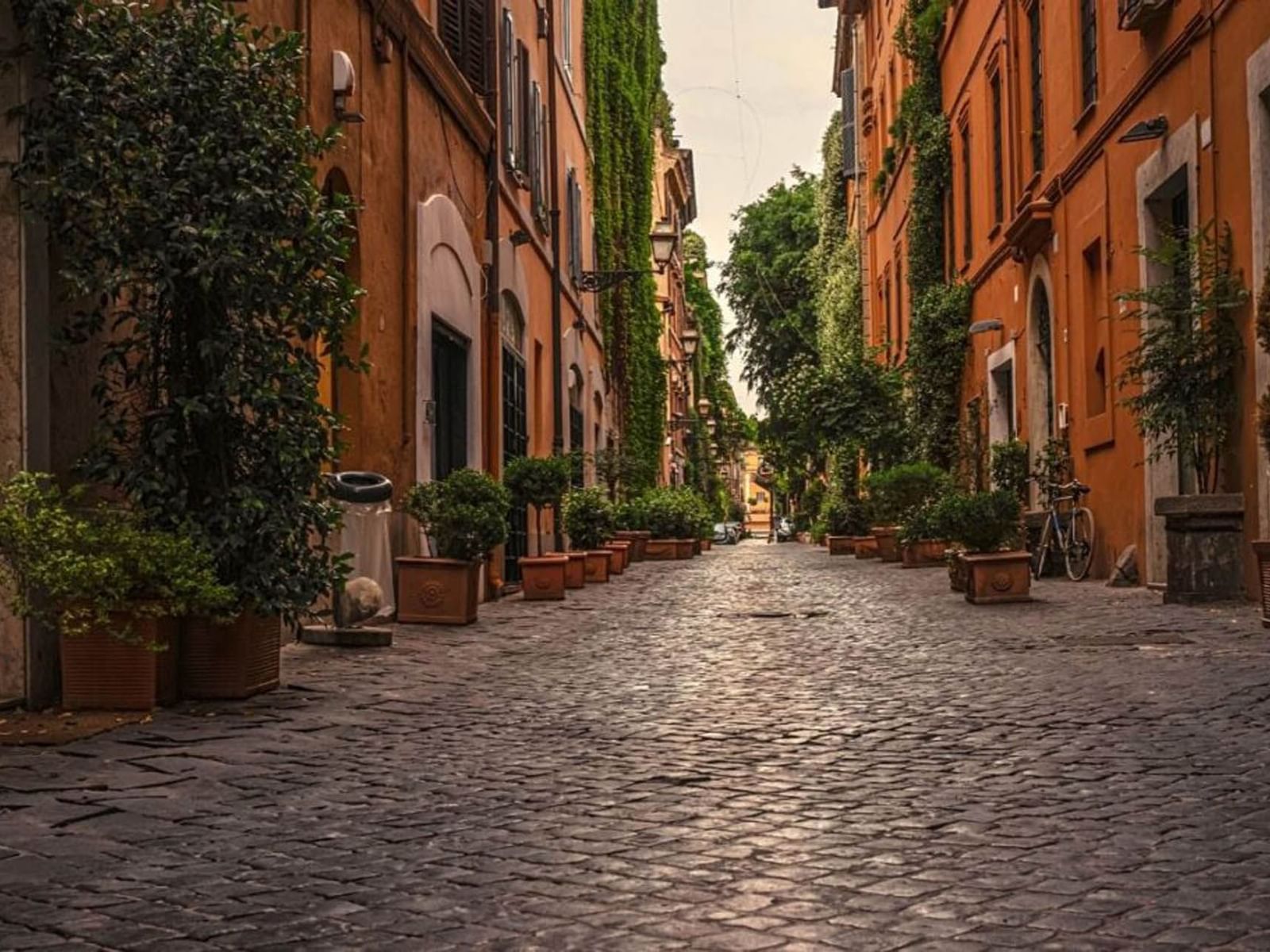 Via Margutta lined with potted plants and orange buildings, leading towards a distant street near The Glam Hotel
