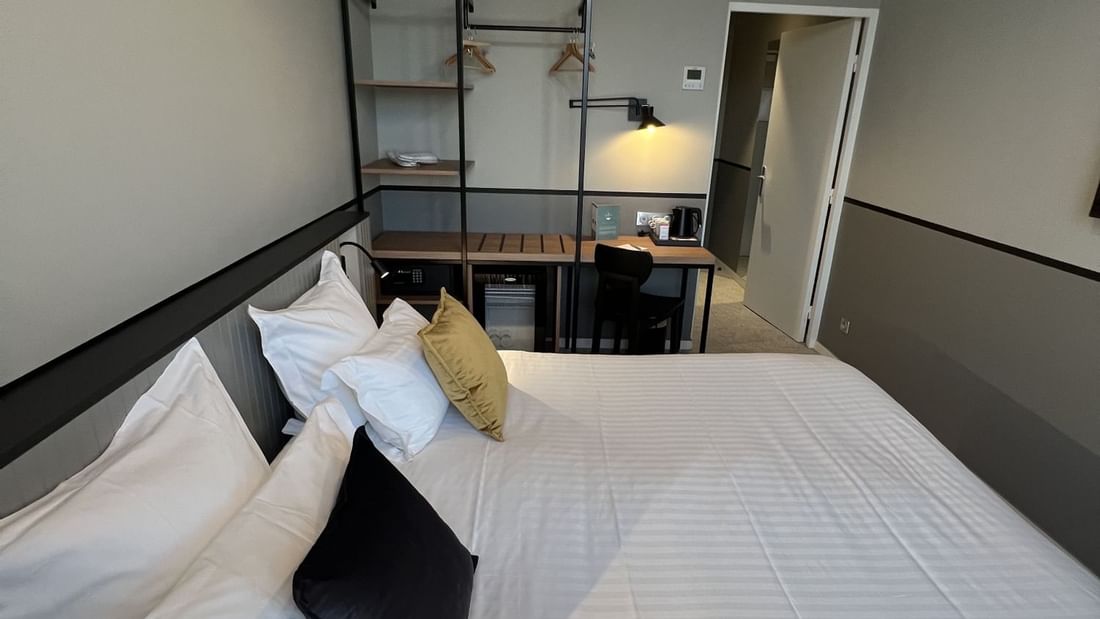 A bedroom with a large bed, pillows, and a desk area with a chair and lamps.