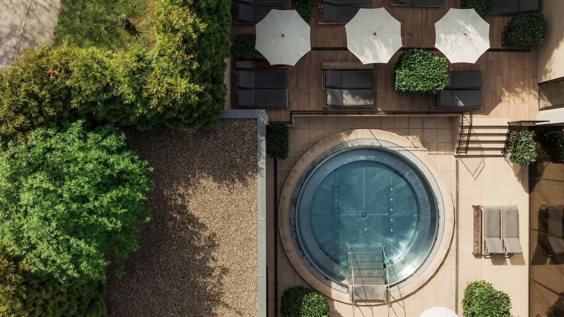 Vista aerea di una piscina rotonda circondata da piante e ombrelloni su un terrazzo.