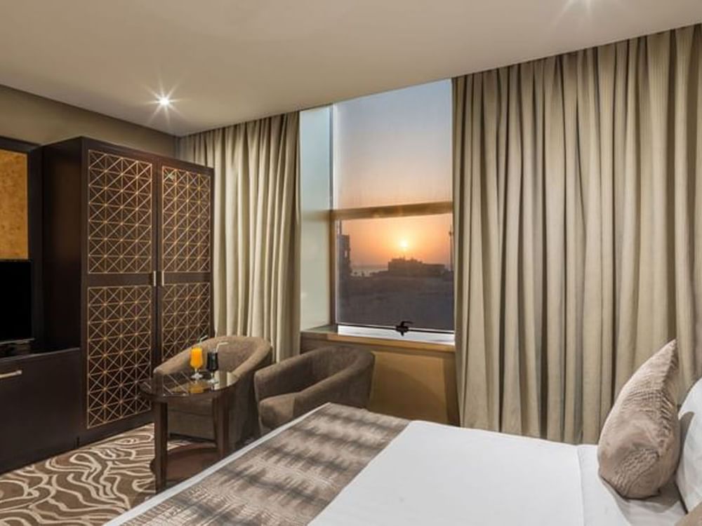 Double bed by a patterned headboard under warm spotlights in Deluxe King Sea View / Twin t Naviti by Warwick Al Khobar