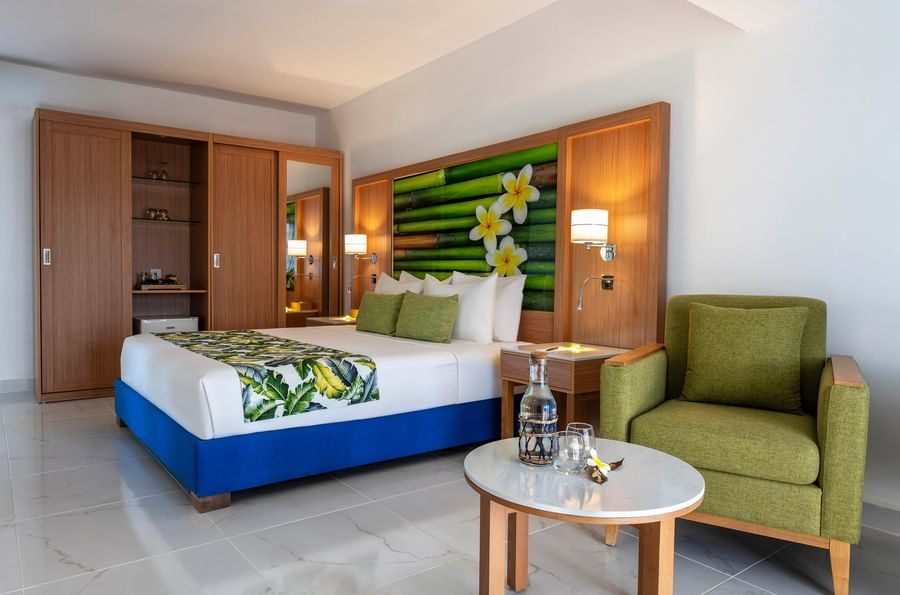 Elegant hotel room with tropical decor, featuring a large bed, armchair, and round table at Warwick Le Lagon - Vanuatu.