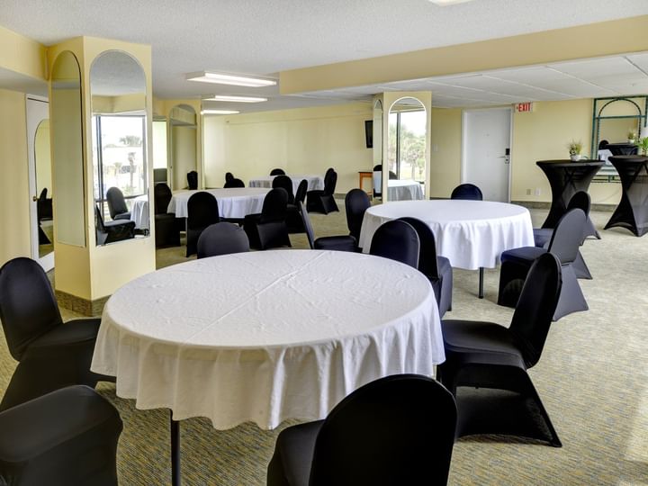 A meeting room with round tables, white tablecloths, and black chairs.