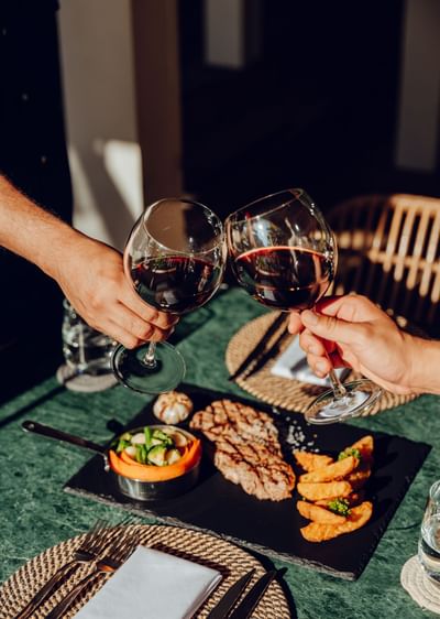 Two people toasting with red wine over a steak dinner in Azure Restaurant & Bar at Barefoot Cay Resort & Marina