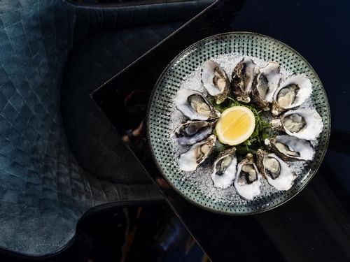A plate of fresh oysters with lemon on a blue textured table in Restaurant Bistro Suzette at Sofitel Brisbane Central