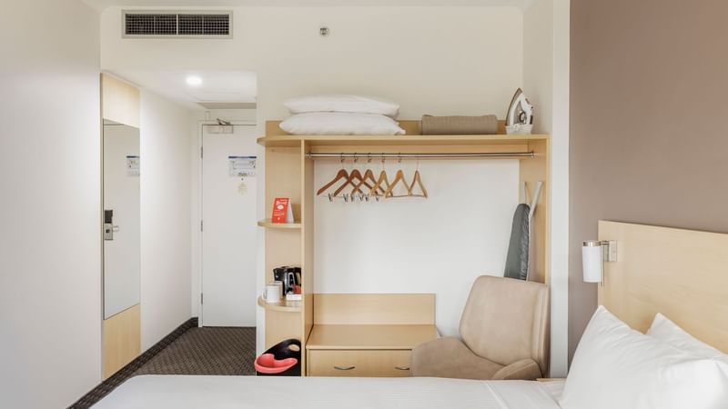 Comfy chair and closet with hangers by the bed in Standard King Room at Novotel Sydney Olympic Park