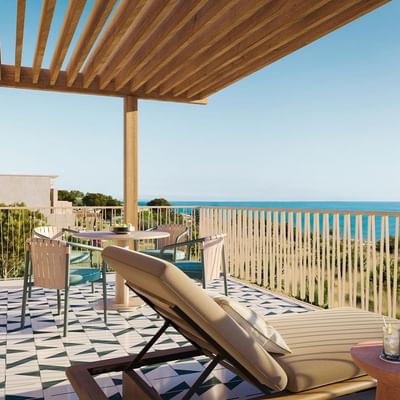 Balcone con vista mare, tavolo, sedie, e chaise longue su pavimentazione geometrica.