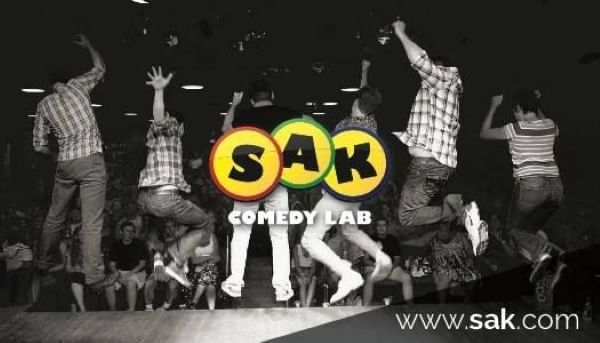 Six people mid-air facing an audience in a black and white photo with the logo for SAK Comedy Lab in color across the middle. 