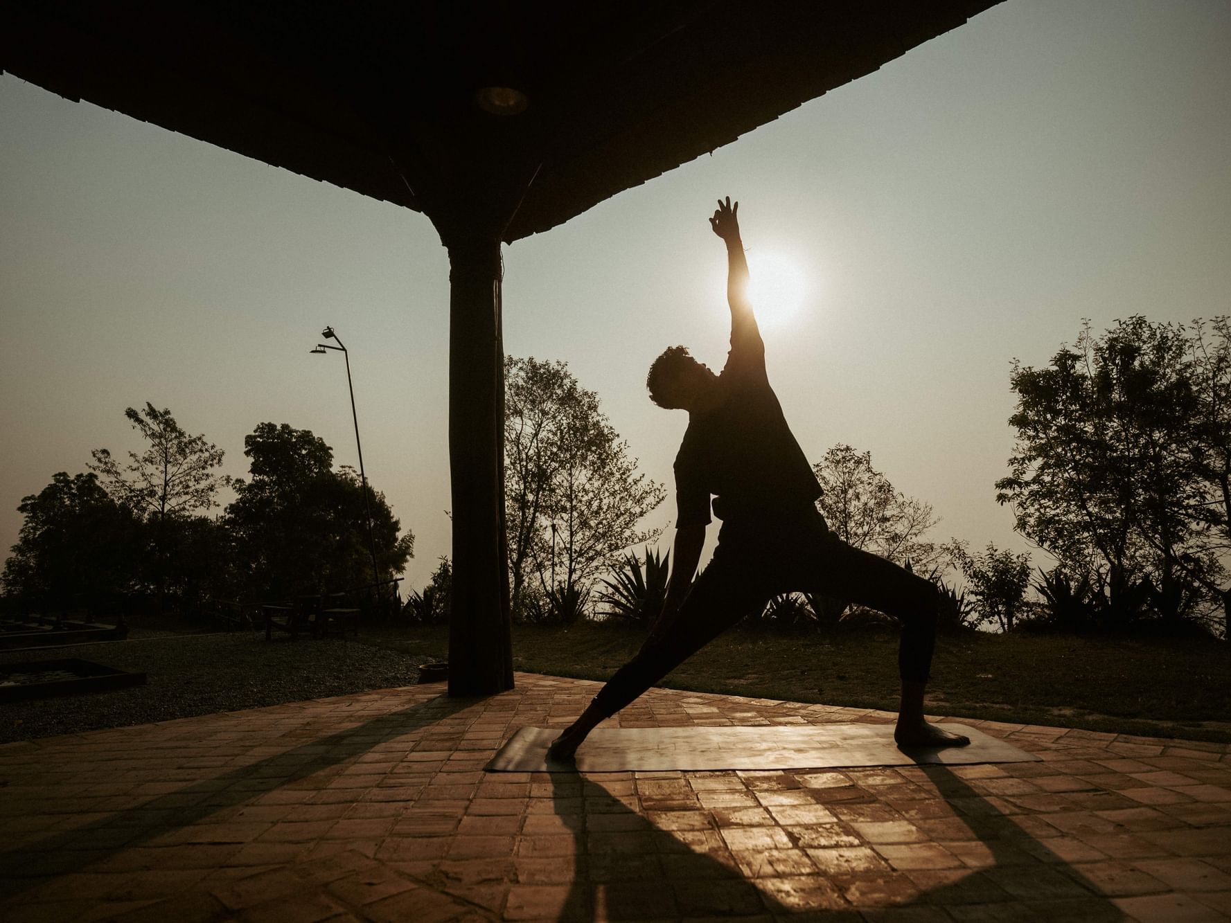 Silhouette of a person practicing yoga at sunset in an outdoor setting near Dwarika's Himalayan Wellbeing