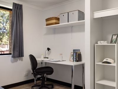 A neat bedroom with a desk, chair, shelf, and closet at UniLodge at Curtin University.