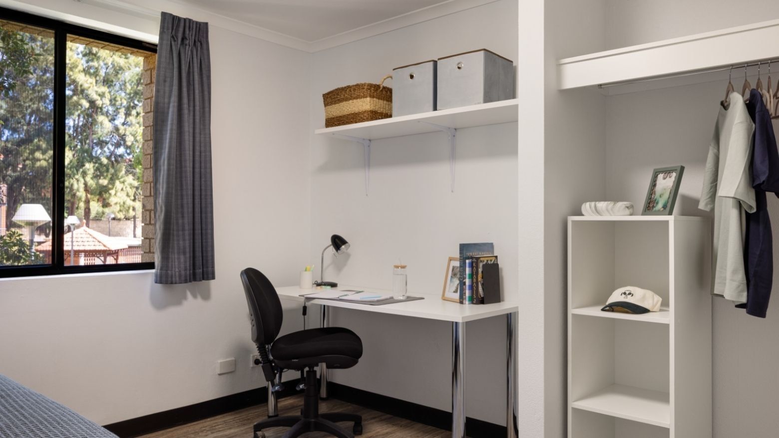 A neat bedroom with a desk, chair, shelf, and closet at UniLodge at Curtin University.