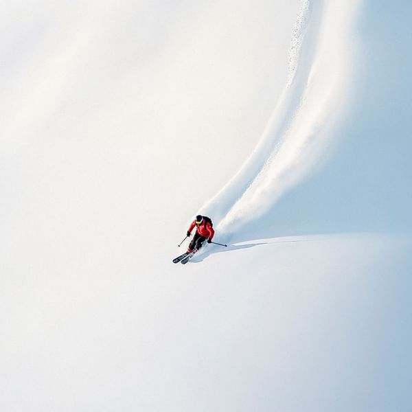 Skifahrer in roter Jacke und schwarzer Hose gleitet elegant durch eine Schneewolke.