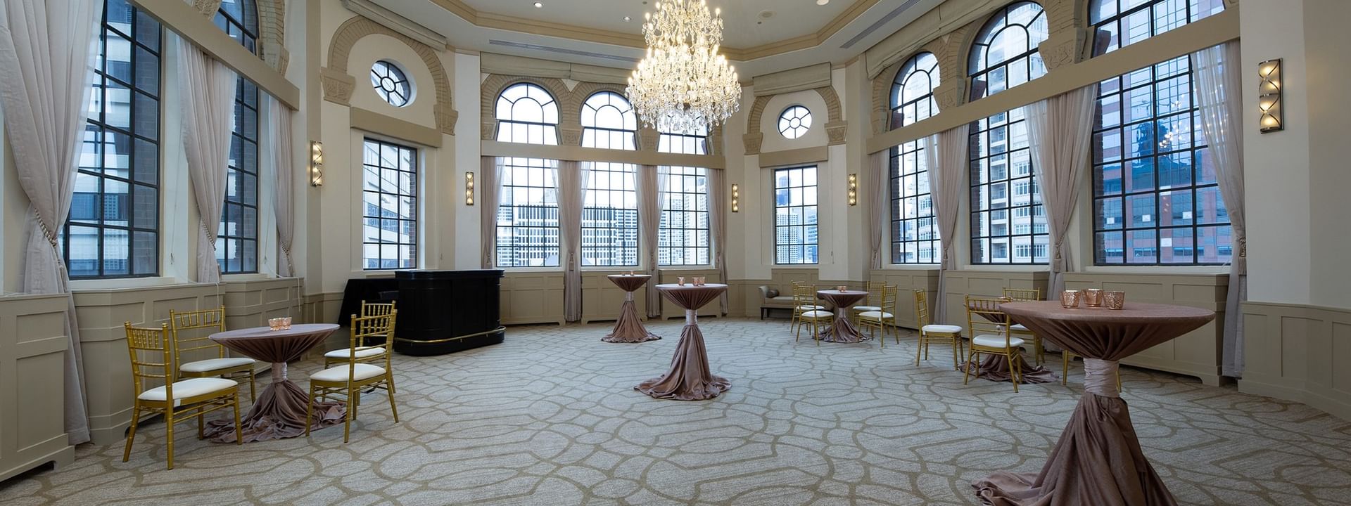 High-top tables with draped cloths, placed by arched windows in Huron Room at Warwick Allerton Chicago