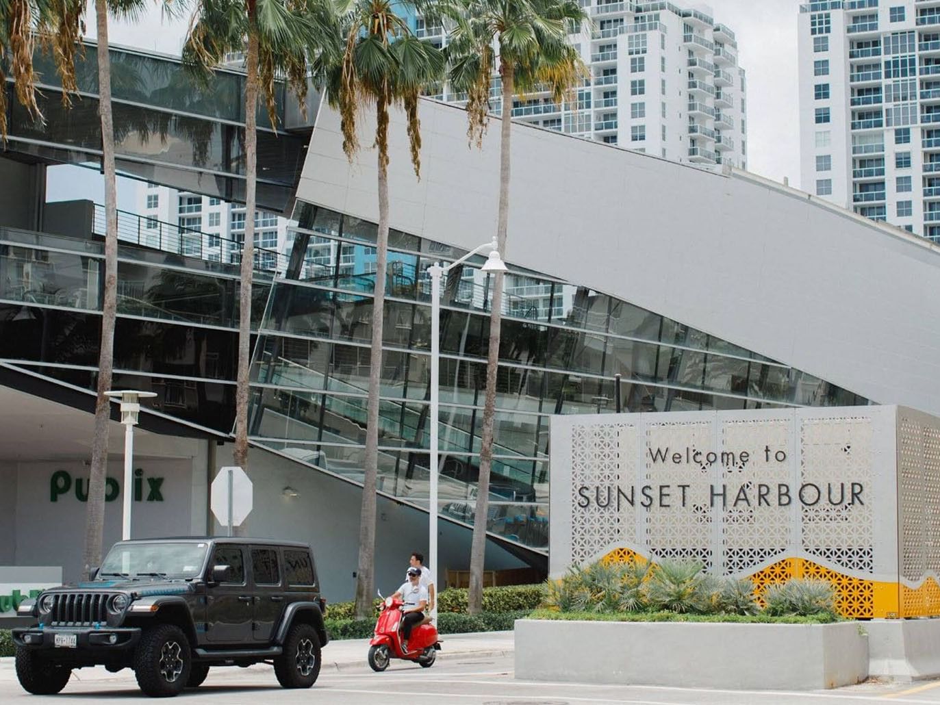 Entrance sign welcoming visitors to Sunset Harbour neighborhood with modern buildings near Tradewinds Apartment Hotel