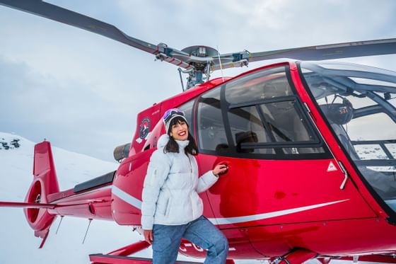 Woman standing by red helicopter for Heli Skiing near Blackcomb Springs Suites