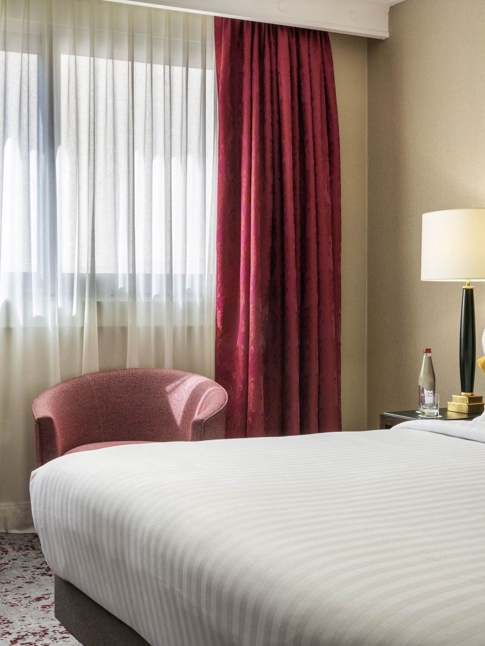 Superior Room with red armchair by a round black table under a white floor lamp near a bed at Warwick Paris Champs Elysées