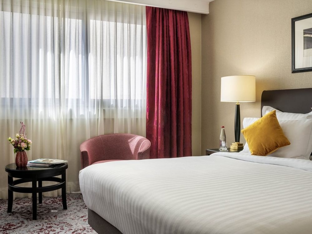 Red armchair by a black round table under red curtains near a white bed in  Superior Room at Warwick Paris Champs Elysées