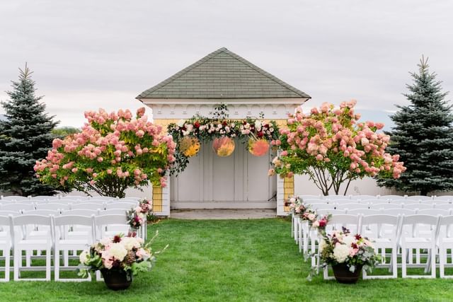 Rows of white chairs by pink hydrangea trees, near a floral-draped pavilion at Mountain View Grand Resort & Spa