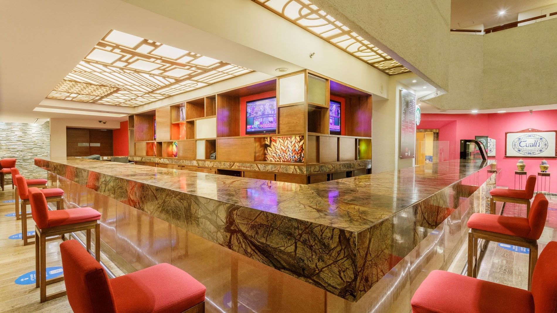 Lobby Bar counter with red stools and built-in TV monitors at Camino Real Aeropuerto Mexico