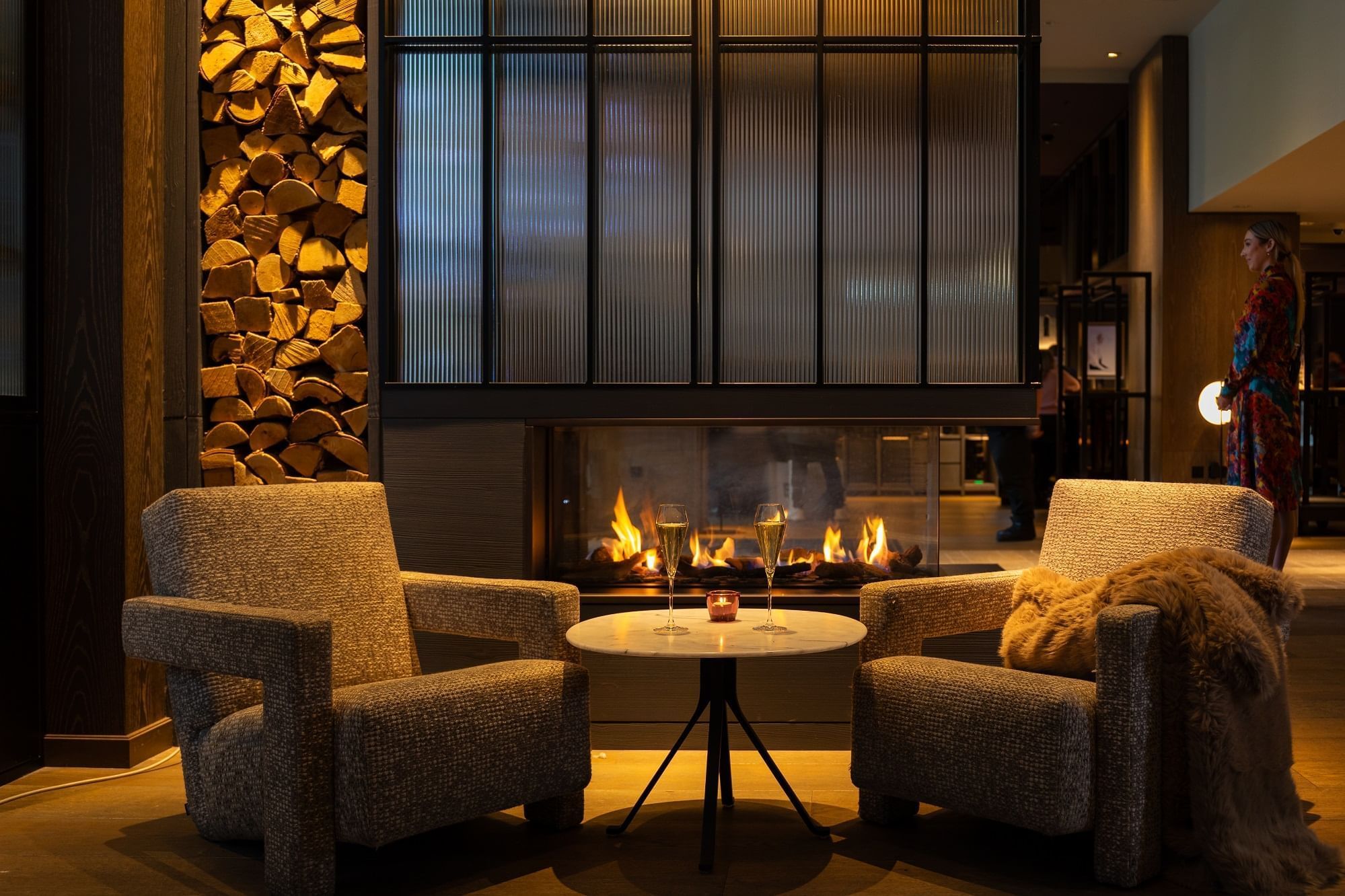 Cozy lounge at The Londoner with two armchairs, a small table holding champagne flutes, and a warm fireplace