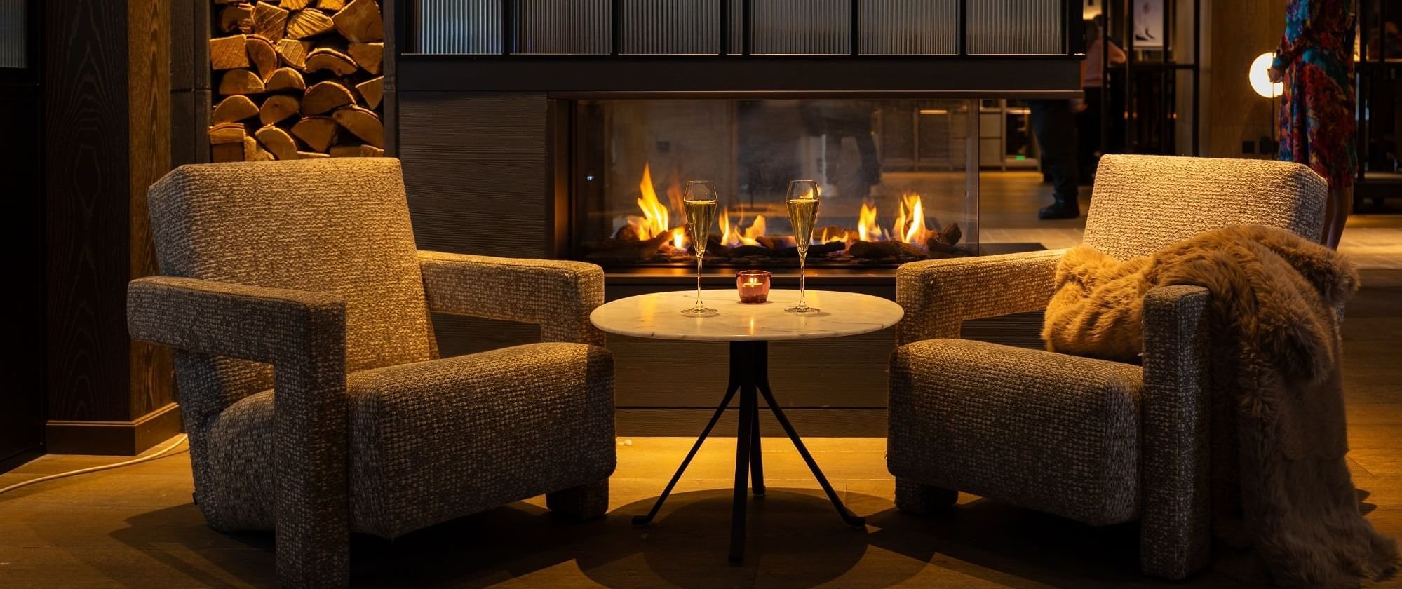 Cozy lounge at The Londoner with two armchairs, a small table holding champagne flutes, and a warm fireplace
