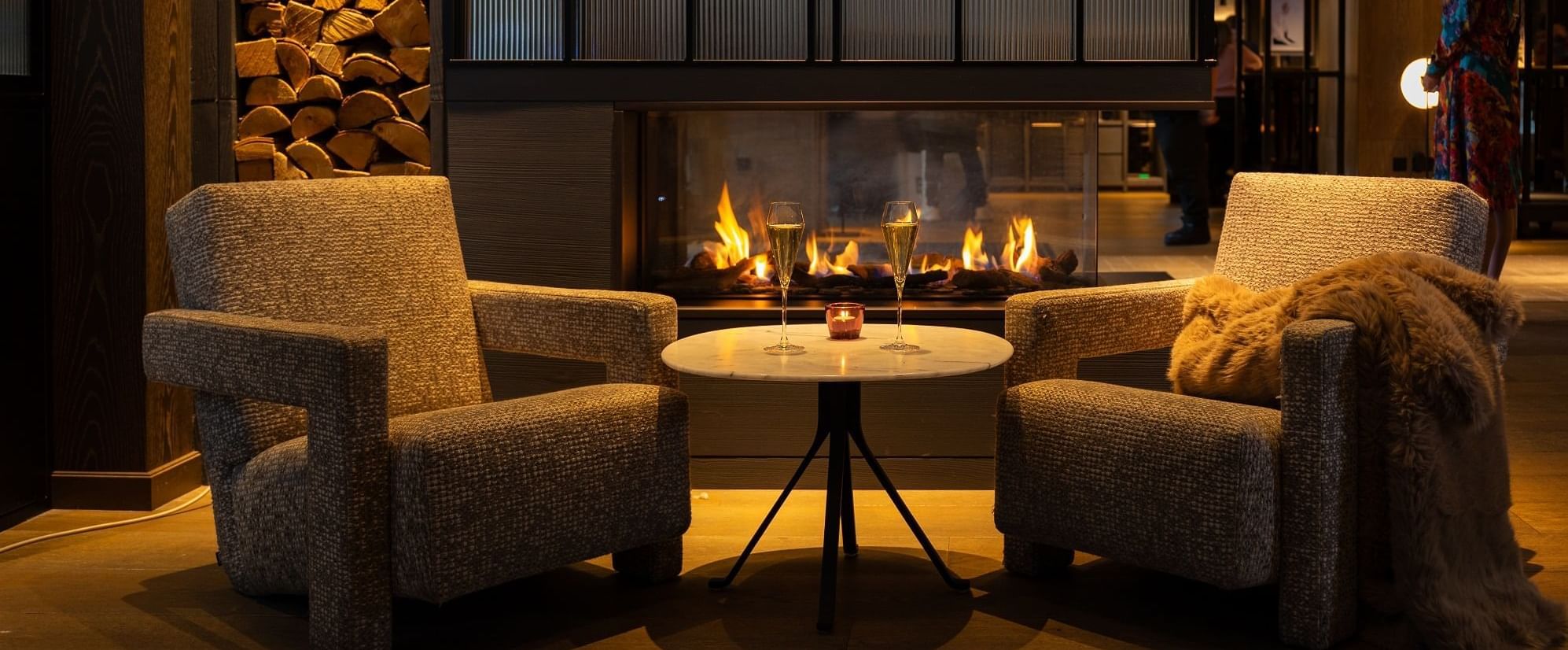 Cozy lounge at The Londoner with two armchairs, a small table holding champagne flutes, and a warm fireplace