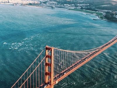 Aerial view of Golden Gate Bridge spanning the bay, with lush green hills and shoreline in the background near Hotel Bijou