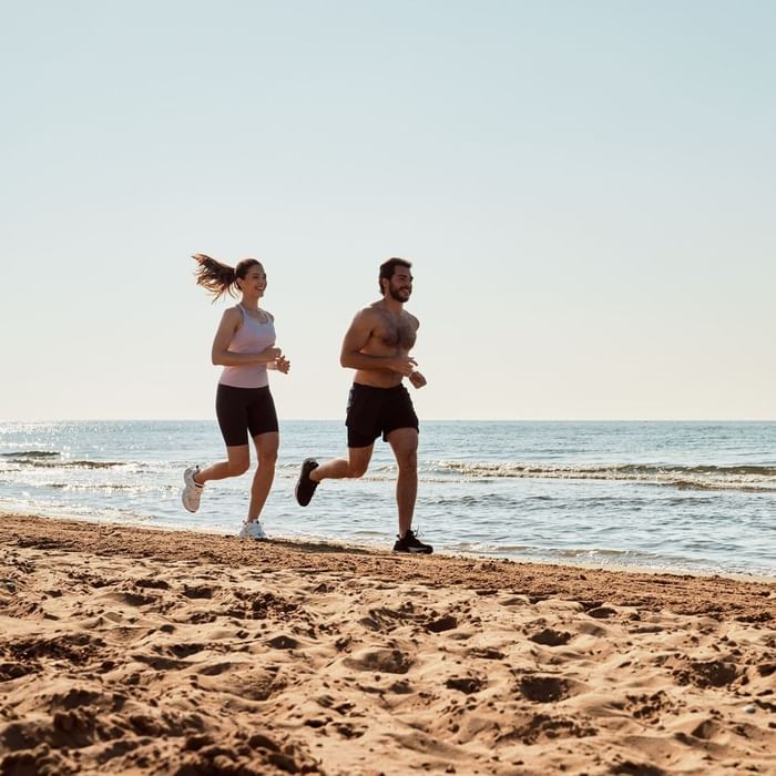 Two people jogging on a sandy beach by the ocean at Falkensteiner Hotel & Spa Jesolo