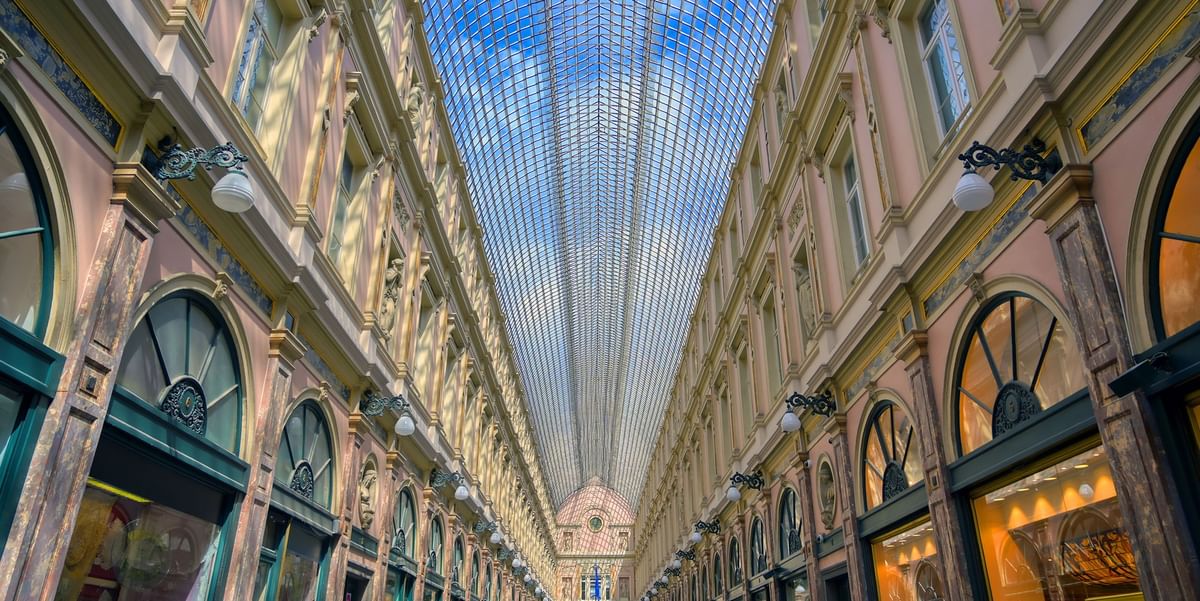 Glass-vaulted ceiling over shopping arcade with ornate pink walls and boutiques near Warwick Grand Place Brussels
