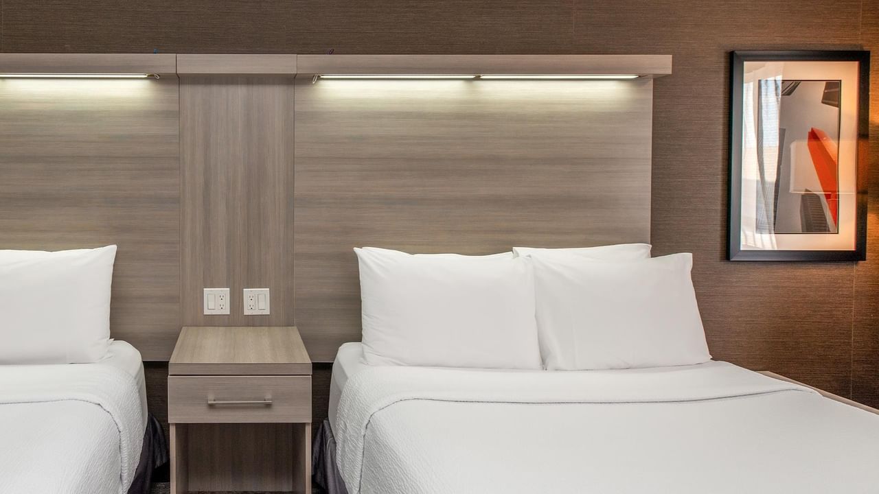 Modern guest room with two beds, white linens, wood-toned accents, and contemporary wall art at Coast Calgary University Area Hotel by APA.