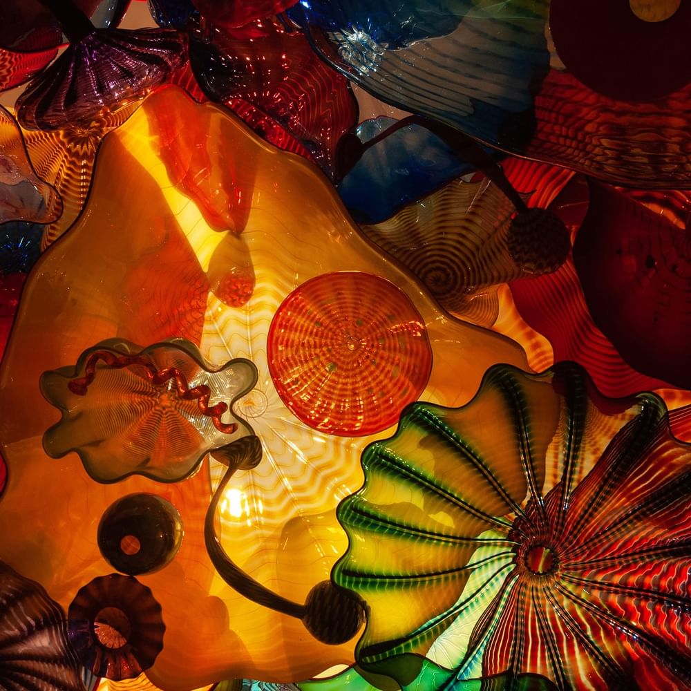 Vibrant glass sculptures featuring orange and green wavy patterns under bright lights at Warwick Seattle
