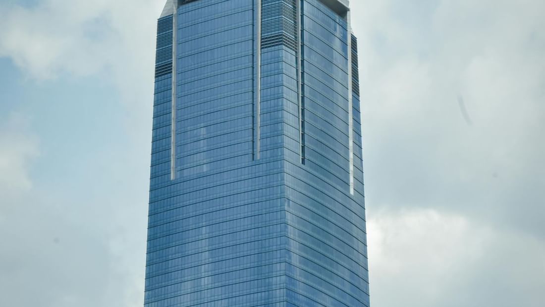 Tall, blue skyscraper with geometric-patterned roof against a partly cloudy sky.