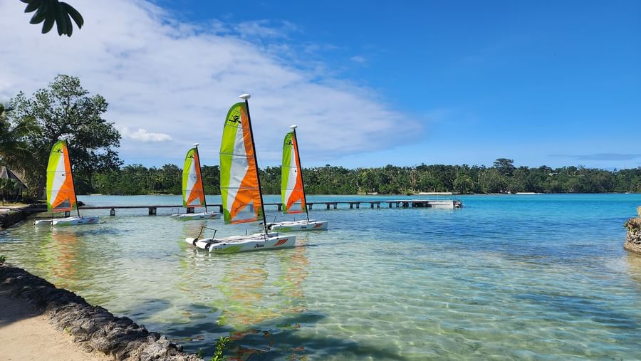 Four catamarans moored near a wooden pier and lush greenery at Warwick Le Lagon Vanuatu.