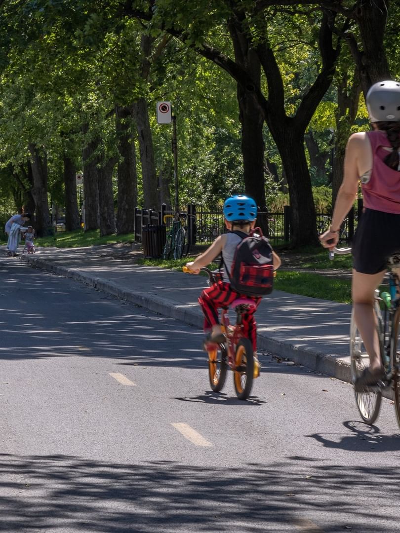Mother and son biking on a lush tree-lined path near the park at Warwick Le Crystal Montreal