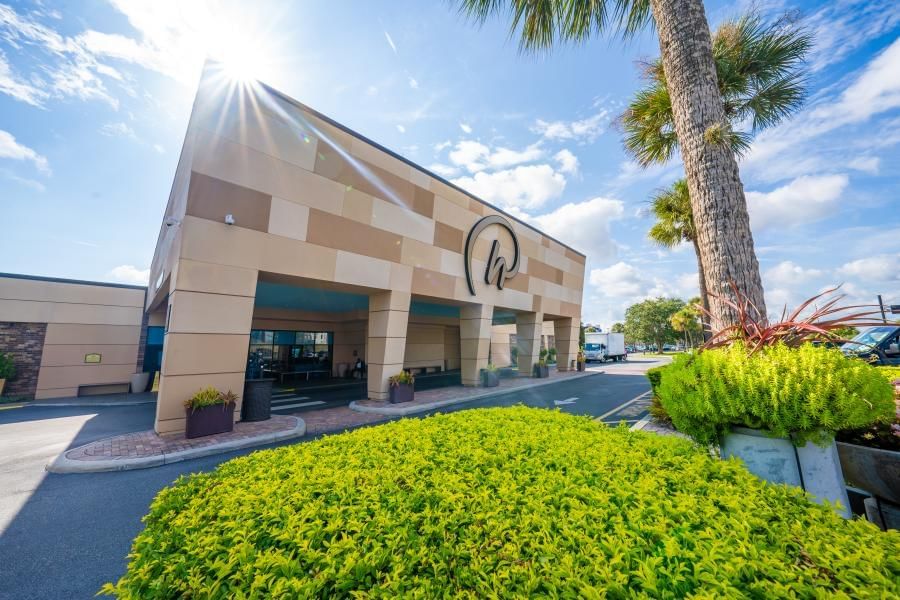 The front of Rosen Inn International with green landscaping and palm trees against a blue cloudy sky. We have the best tips for visiting Universal.