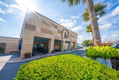 Modern hotel entrance with palm trees and bright green landscaping under sunny blue skies at Rosen Inn International