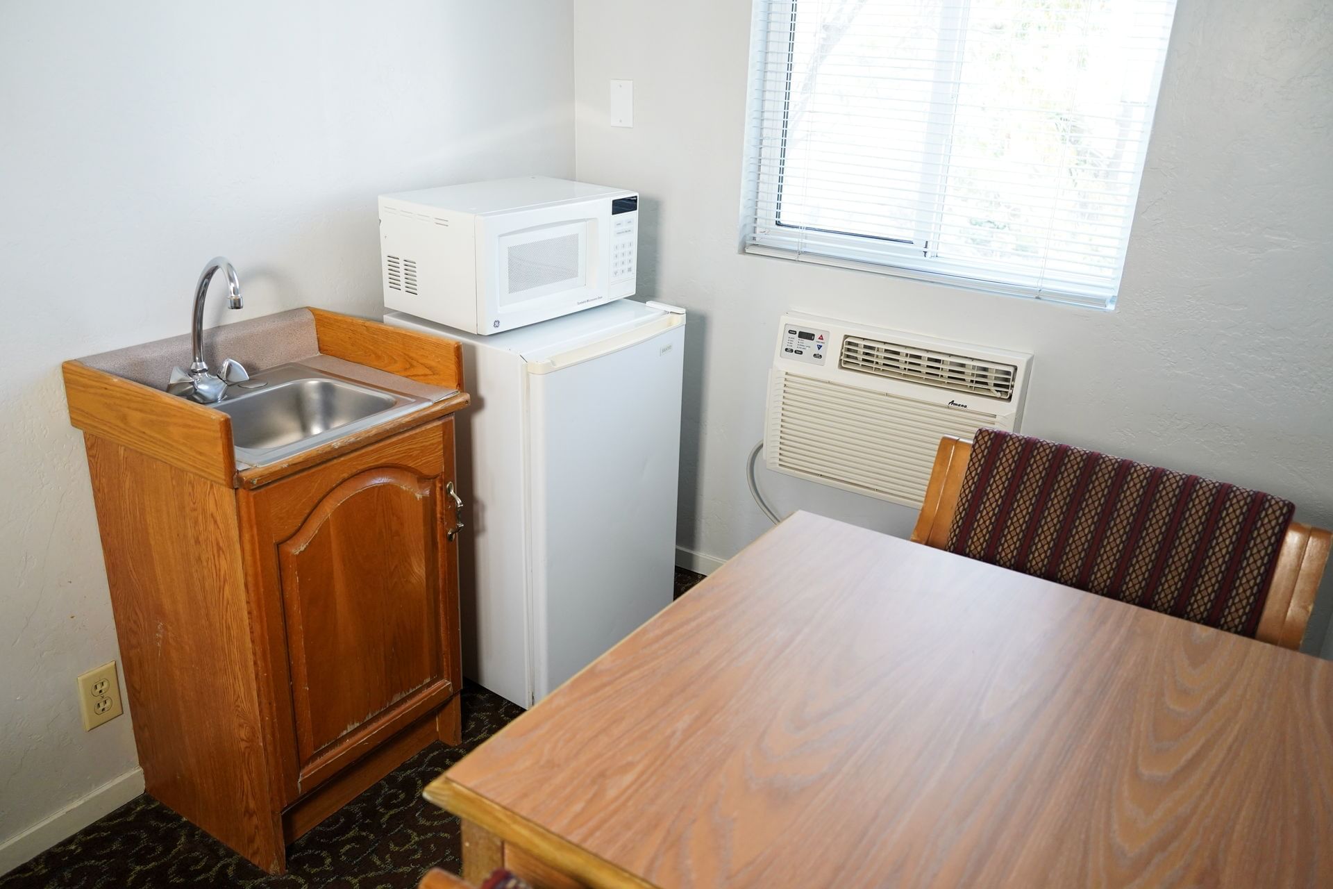 A compact kitchenette with sink, microwave, and mini fridge, adjacent to a dining area with a table and chairs.