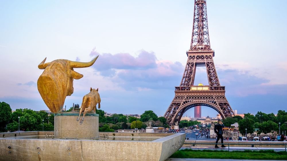 Golden bull statues by a stone fountain under the Eiffel Tower at sunset at Warwick Paris Champs Elysées