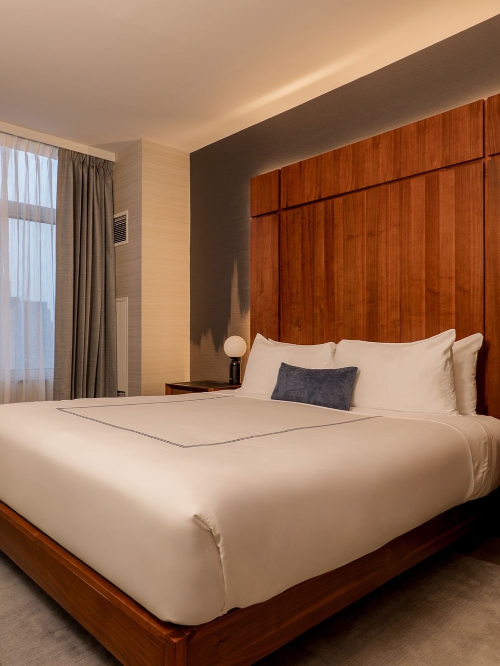 Modern bedroom with white bedding, wood headboard, gray curtains, and bedside lamps at Gansevoort Meatpacking NYC - NEW