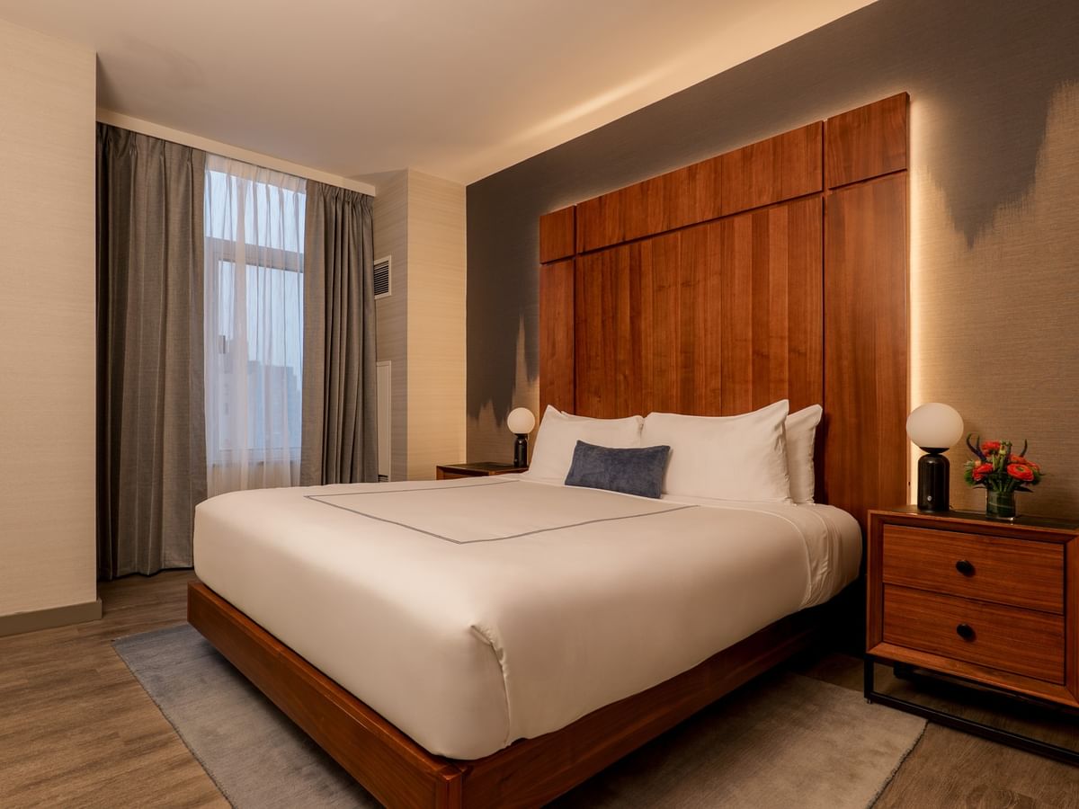 Modern bedroom with white bedding, wood headboard, gray curtains, and bedside lamps at Gansevoort Meatpacking NYC - NEW