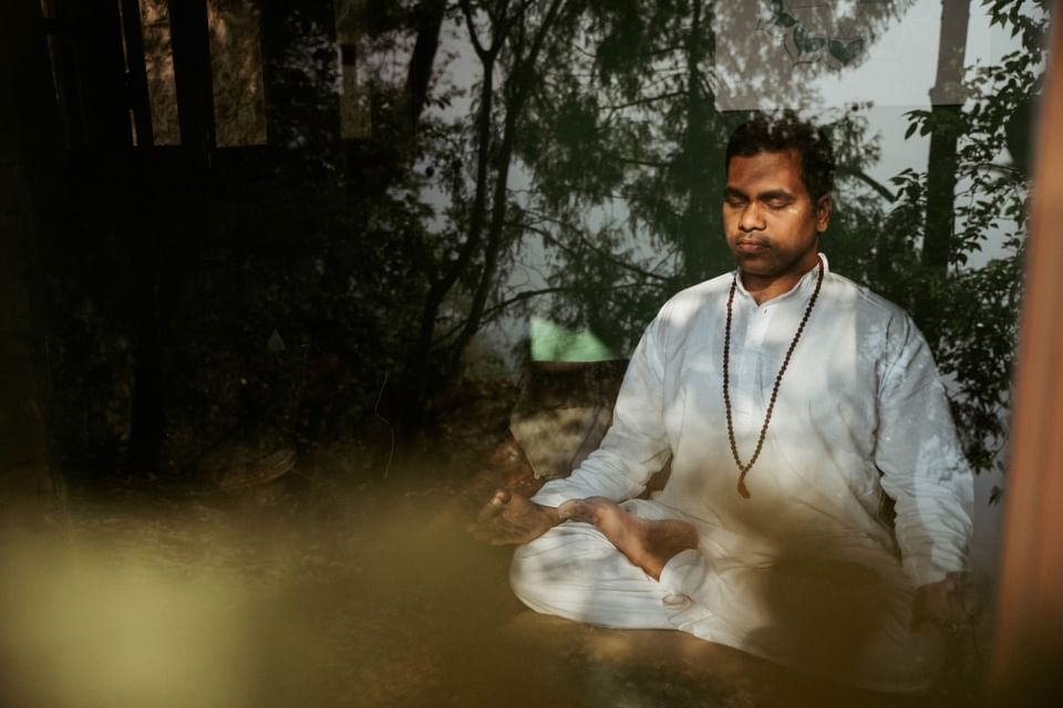 Person in white meditating among trees and soft light reflections in Pancha Kosha Himalayan Spa at Dwarika's Hotel Kathmandu