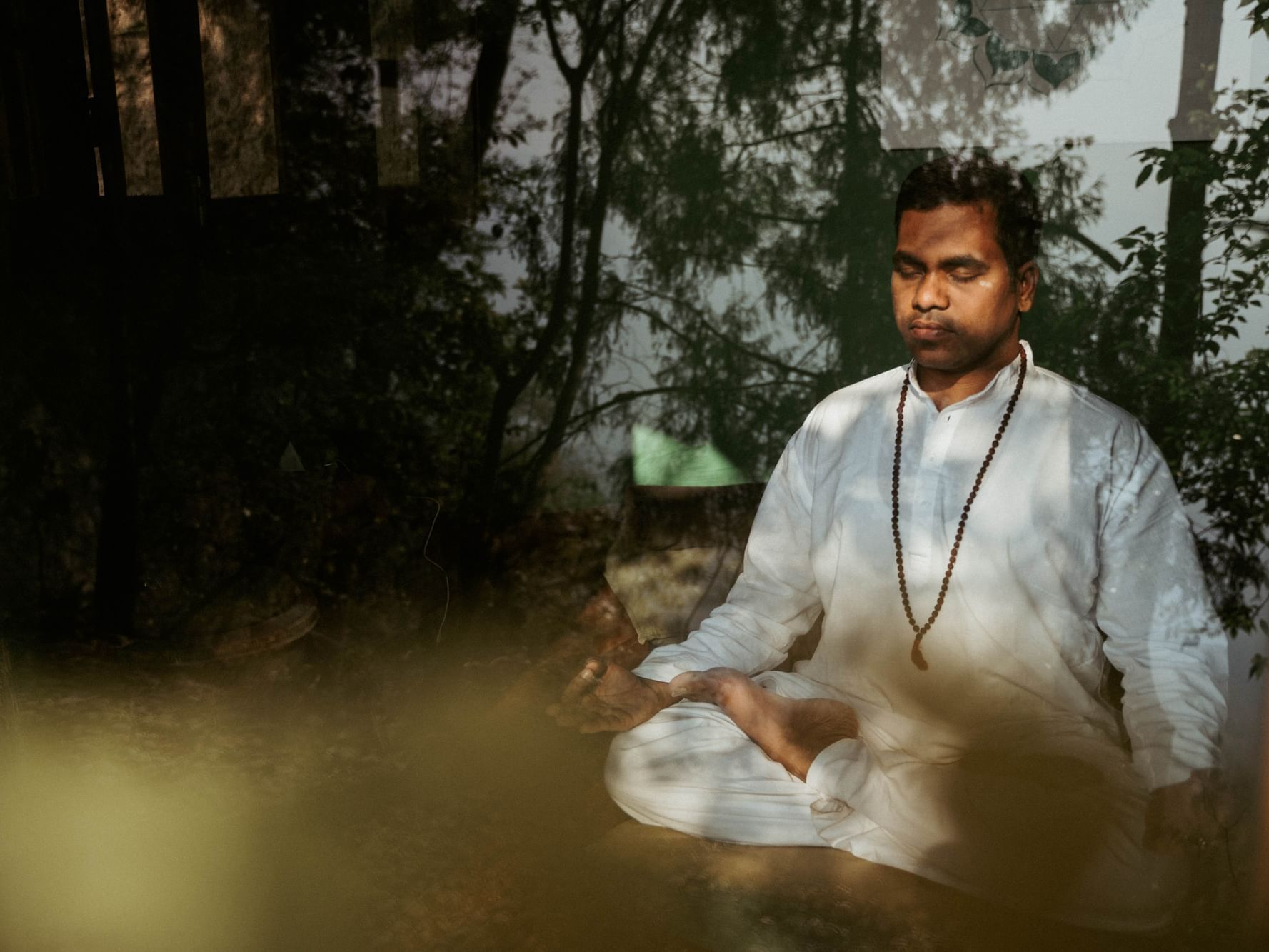 Person meditating with a prayer bead necklace, surrounded by a serene natural setting at Dwarika's Himalayan Wellbeing
