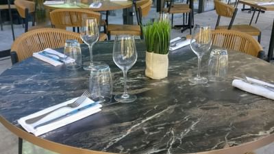 Table ronde en marbre avec chaises en osier et ustensiles de table dans un restaurant avec vue sur l'extérieur.