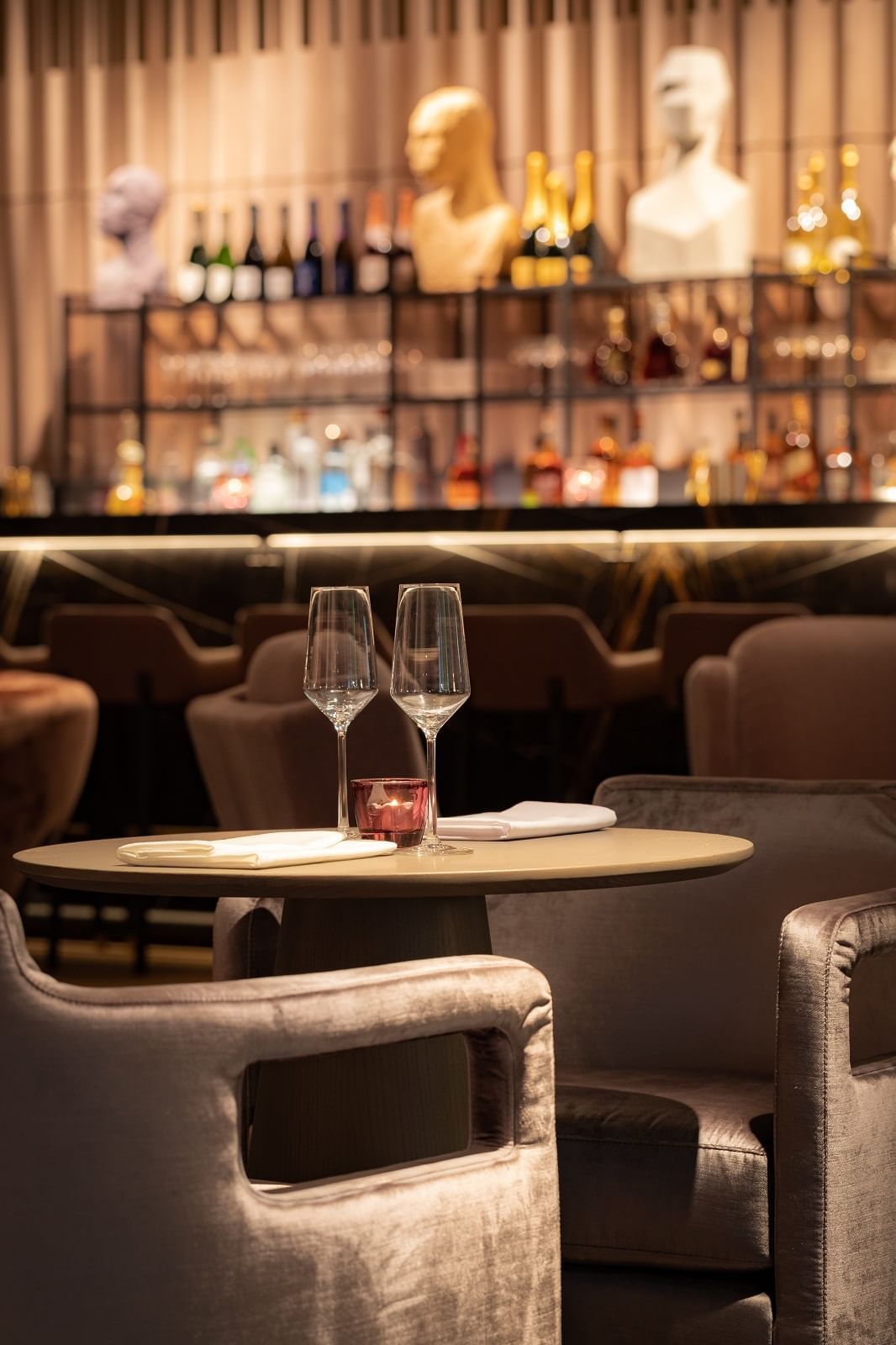 Gros plan sur une table dressée avec des verres et un comptoir de bar en arrière-plan flou, dans « The Stage » de l'hôtel The Londoner