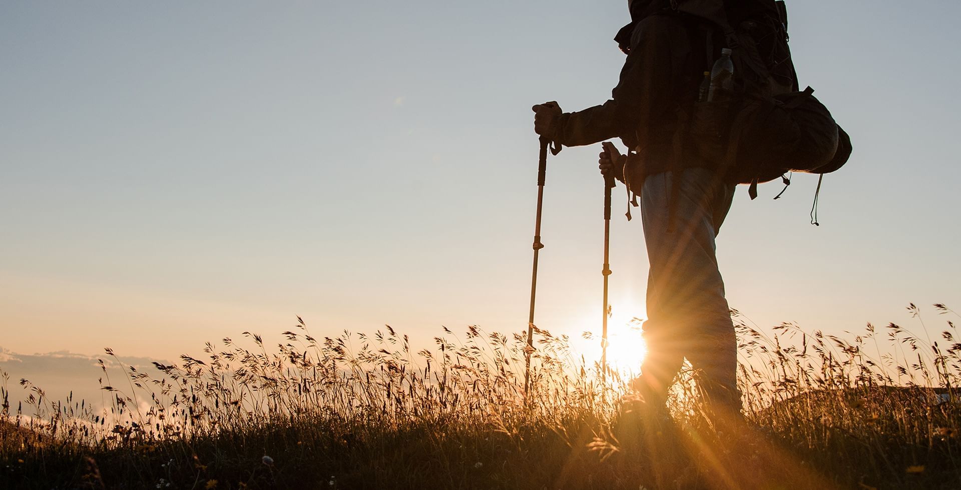hiker standing in tall grass with sun low in the sky