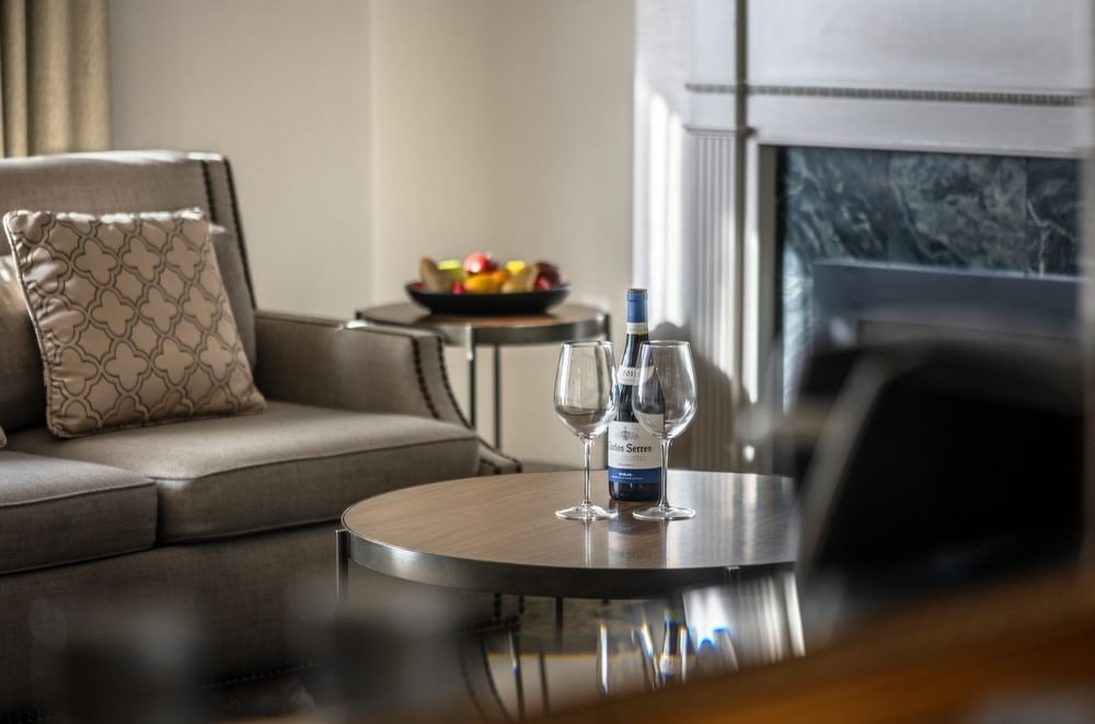 Wine and glasses on a wooden table by a grey armchair near a fireplace in Balcony Junior Suite at Warwick San Francisco