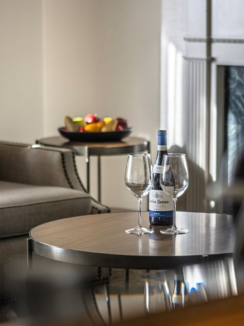 Wine and glasses on a wooden table by a grey armchair near a fireplace in Balcony Junior Suite at Warwick San Francisco